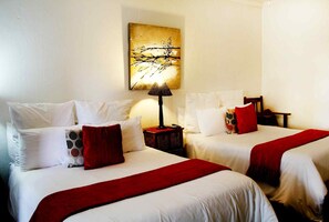 Une chambre d’hôtel avec deux lits, chacun agrémenté de draps blancs et de touches de couleur rouge, une lampe et un tableau au mur.