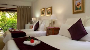 Une chambre d’hôtel avec deux lits, chacun agrémenté de draps blancs et d’oreillers violets. On y trouve deux tables de chevet avec des lampes, une petite table avec un vase et un balcon avec une table et des chaises.