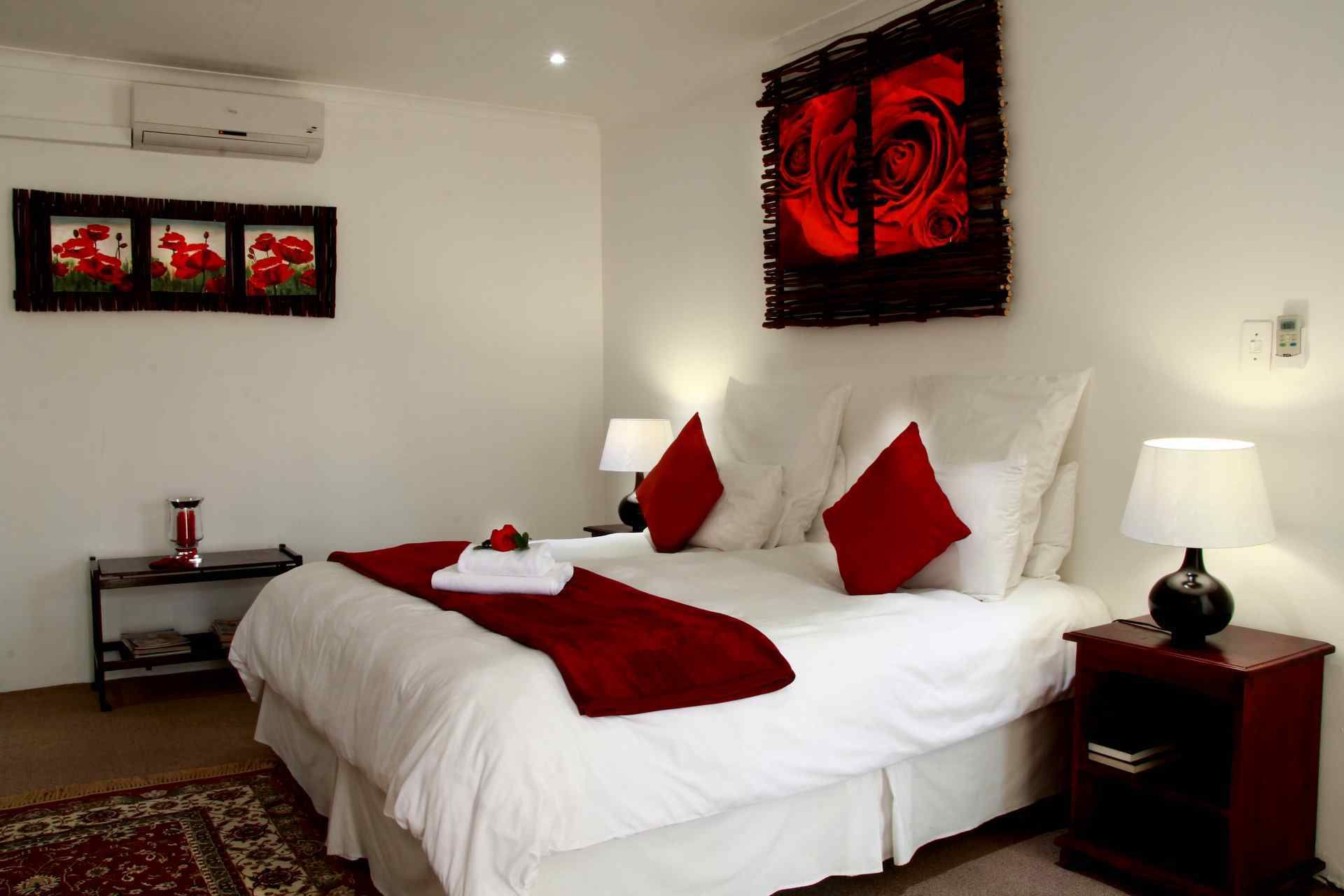 Een hotelkamer met een bed, rode kussens, een rode plaid, een rode roos, een rode lamp, een nachtkastje, een rode vaas en een rode wanddecoratie.