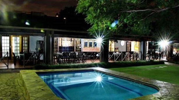 Un espace piscine avec une piscine à eau claire, entouré d’une terrasse couverte dotée de tables et de chaises.