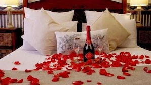 Un lit recouvert de pétales de rose, deux coupes à champagne et une bouteille de champagne.