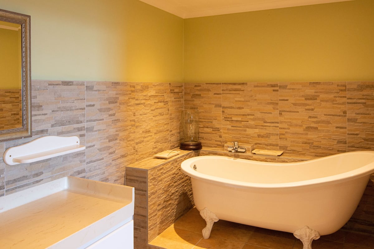 Un baño con una bañera independiente, un tocador con espejo y pared de azulejos.