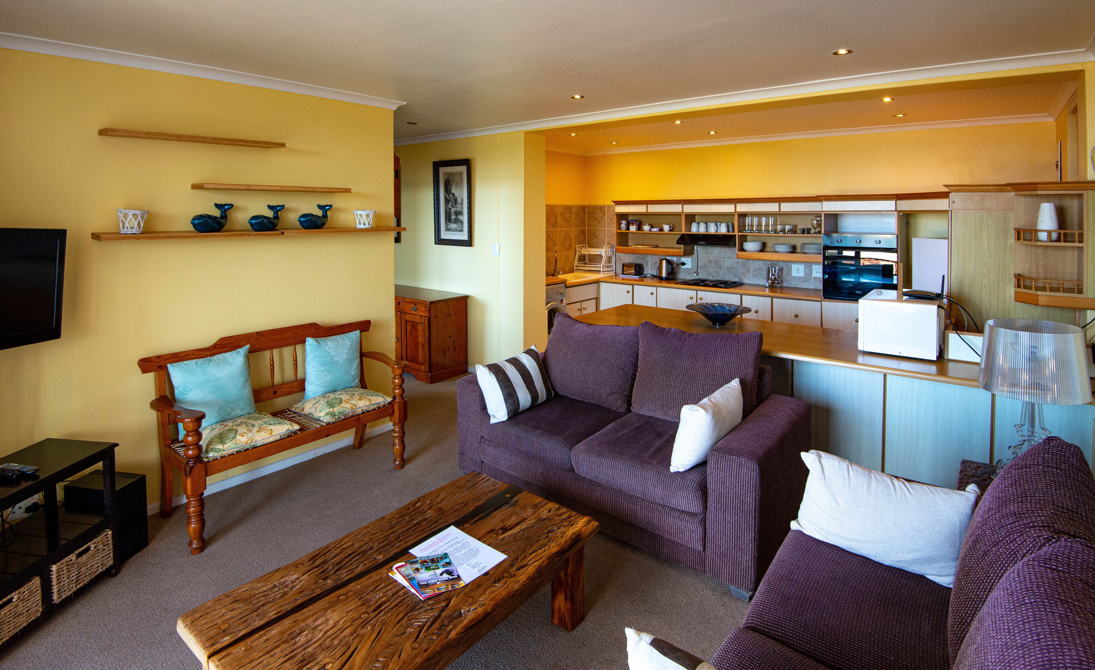 A living room with a sofa, a wooden coffee table, a television, and a kitchen area with cabinets and a countertop.