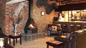 A cozy living room with a fireplace, leather furniture, and a bar area. - Almar Exclusive Game Ranch (Bloemhof)