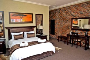 A hotel room with a large bed, a desk, and a brick wall.