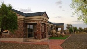 A two-story house with a brick exterior, a covered patio, and a landscaped garden. - Almar Exclusive Game Ranch (Bloemhof)