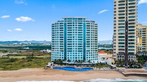 Un hotel frente a la playa con piscina, varios pisos y vista al océano.