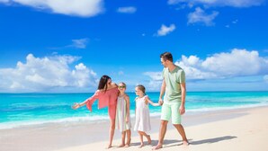 Una familia caminando por una playa con cielos despejados y aguas turquesas.