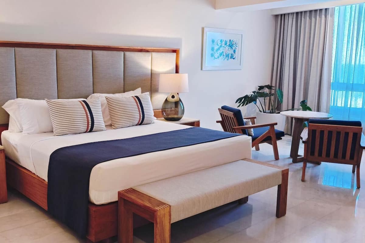 Een hotelkamer met een groot bed, bedlampen, een houten bankje, een kleine tafel en een stoel.