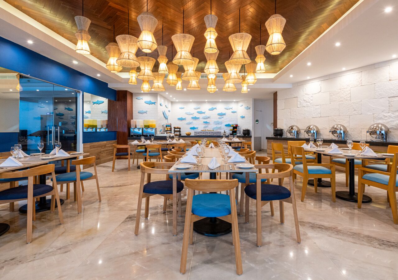 A restaurant with a long communal table, individual tables, and blue cushioned chairs.
