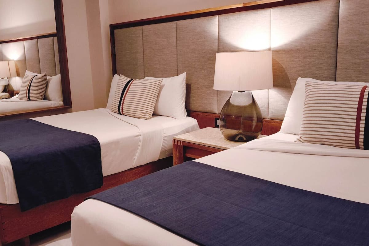 Een hotelkamer met twee bedden, een nachtkastje met een lamp en een spiegel.
