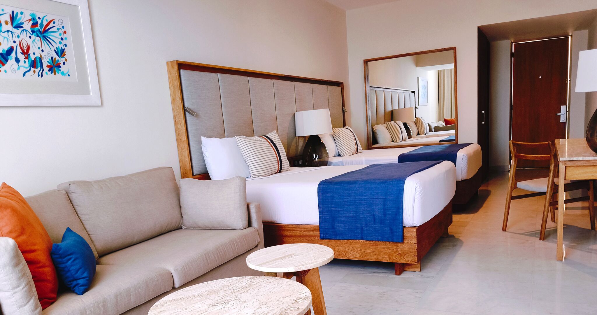 A hotel room with a sofa, two beds, a dining table, and a mirror.