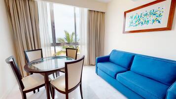 Una habitación con una mesa de vidrio, cuatro sillas, un sofá azul y un ventanal con cortinas.