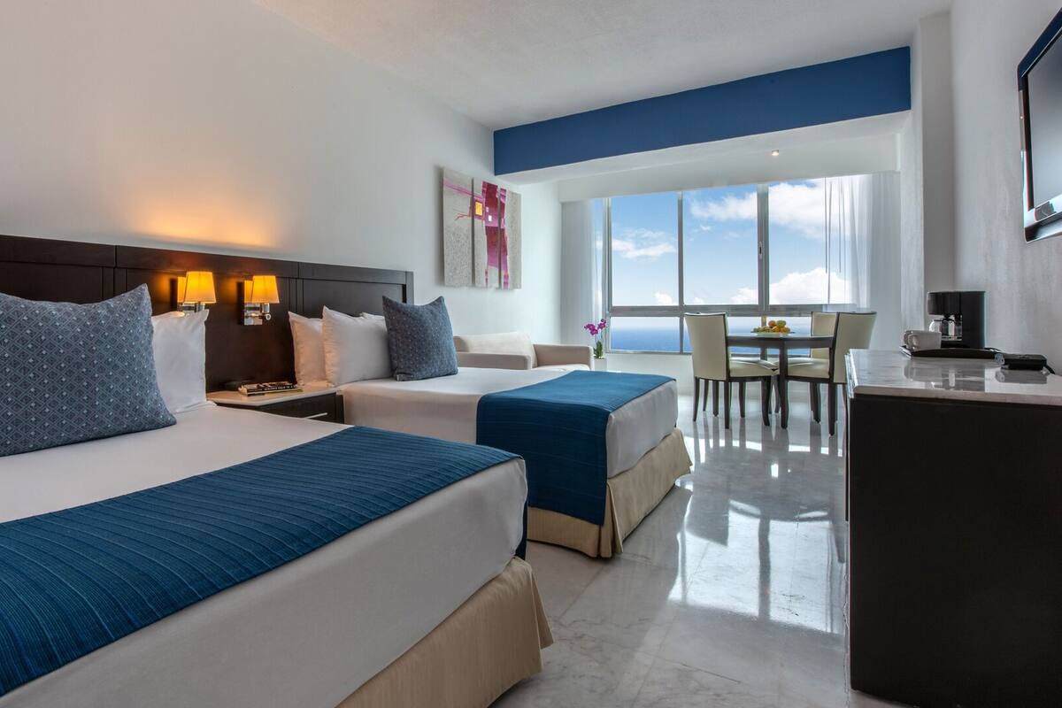 Een hotelkamer met twee bedden, een bureau en uitzicht op zee.