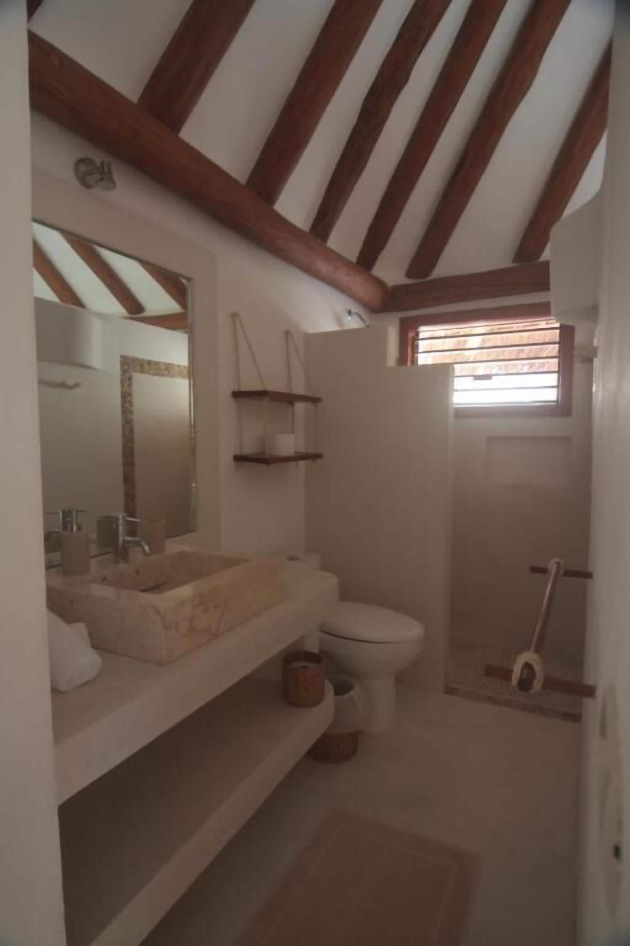 Une salle de bain avec un plafond en bois, un lavabo, des toilettes et un espace douche.