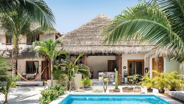 A poolside area with a thatched-roof building, palm trees, and a clear blue pool. - Tierra del Mar Hotel - Adult Only (Isla Holbox)