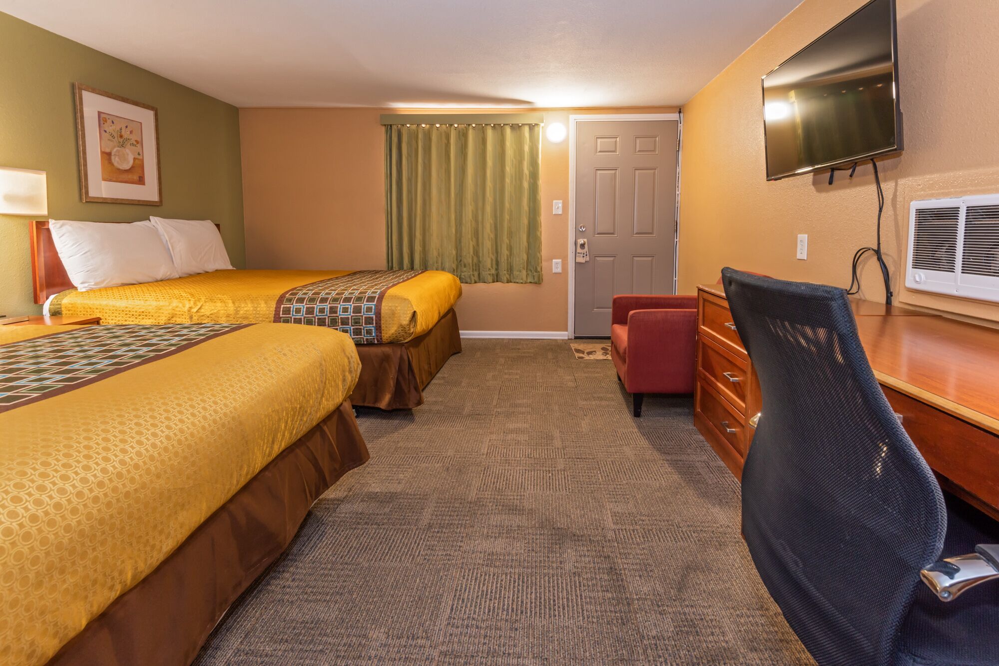A hotel room with two beds, a desk, a chair, a television, and a door.