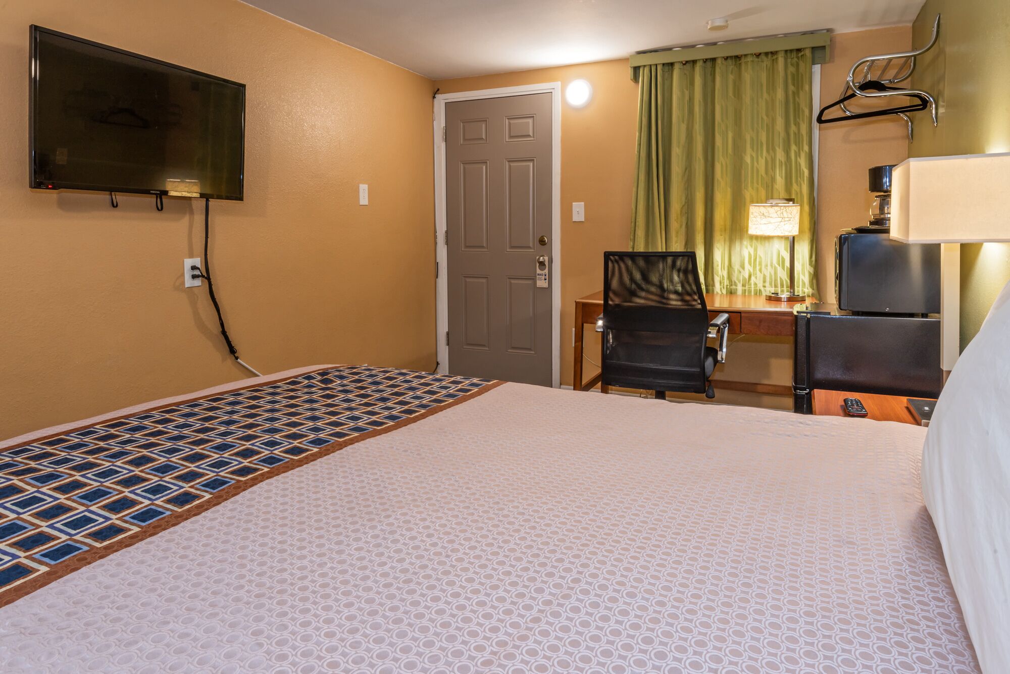 A hotel room with a bed, a desk, a chair, a television, and a lamp.