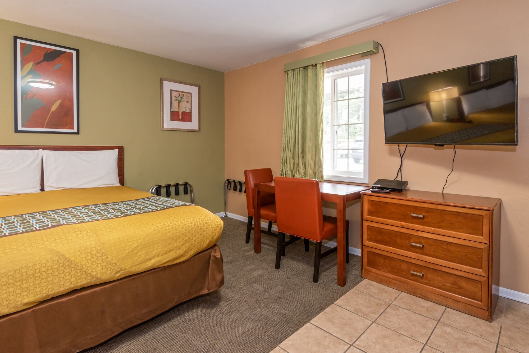 A hotel room with a bed, a desk, a chair, a TV, and a dresser.