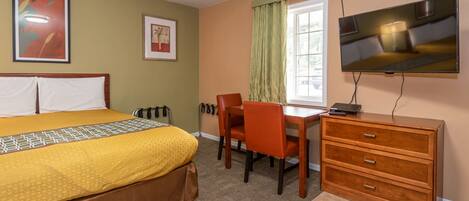 A hotel room with a bed, a desk, a chair, a TV, and a dresser.