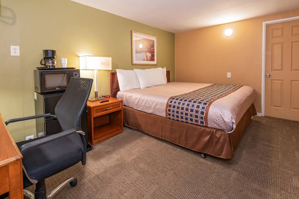 A hotel room with a bed, a desk with a chair, a television, and a lamp.