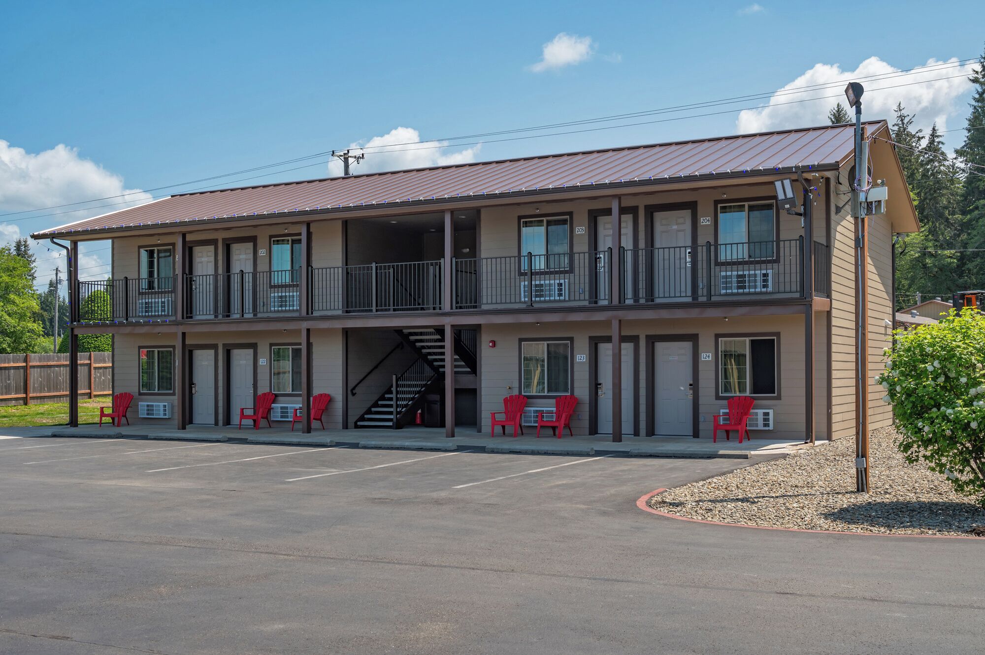 A two-story motel with a covered parking area and red chairs outside.