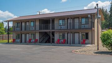 A two-story motel with a covered parking area and red chairs outside.