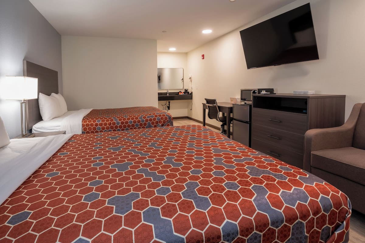 A hotel room with two beds, a desk, a chair, a TV, and a minibar.