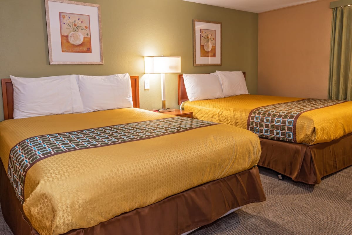 A hotel room with two beds, each with a patterned bedspread and white pillows. There are framed artworks on the walls and a lamp on the nightstand.