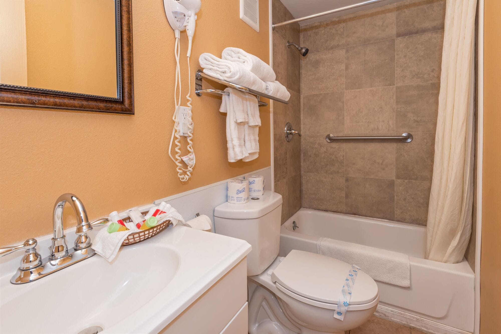 A bathroom with a sink, toilet, and shower. There are towels and toiletries on the counter.