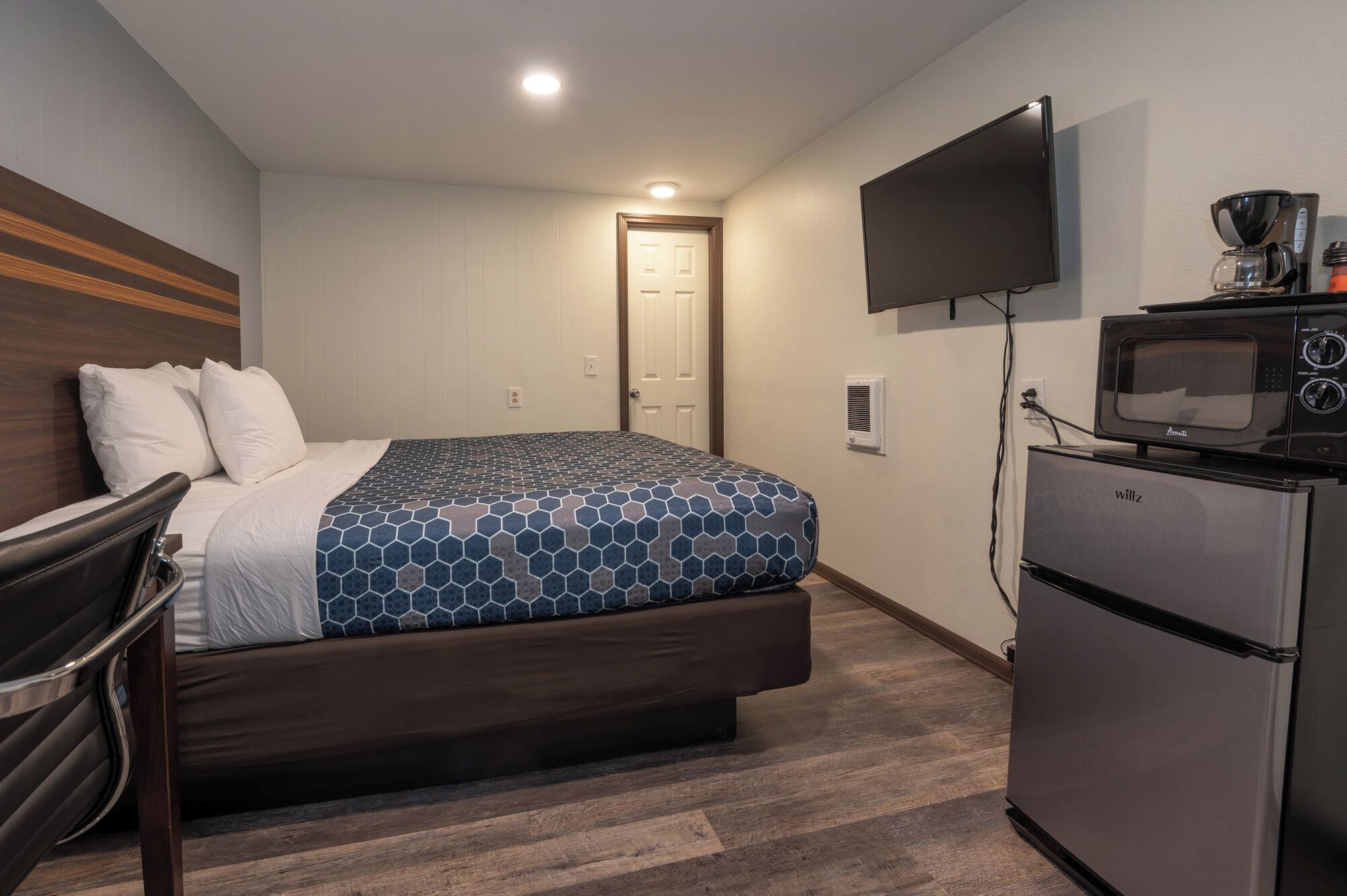 A hotel room with a bed, a TV, a microwave, and a refrigerator.