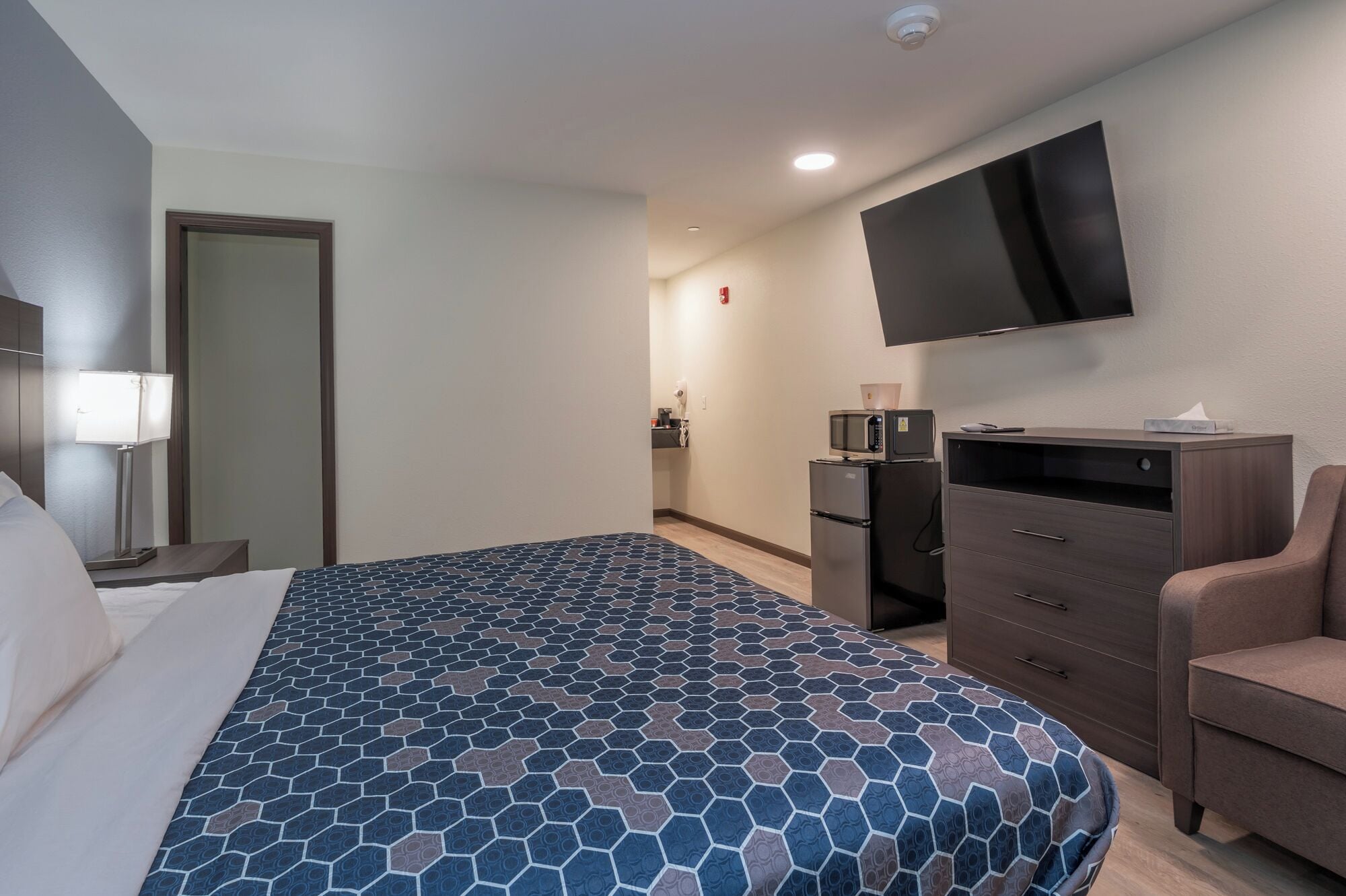 A hotel room with a bed, a desk, a chair, a TV, and a minibar.