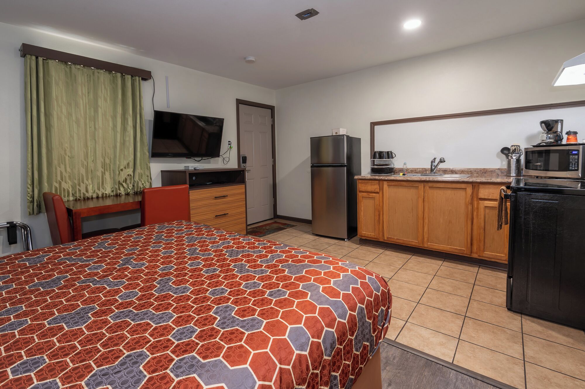 Une chambre d’hôtel de taille réduite, équipée d’un lit, d’une télévision, d’un réfrigérateur, d’un four à micro-ondes et d’une petite kitchenette.