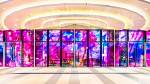 Un edificio moderno con techo curvo y amplios ventanales que muestran arte abstracto colorido.