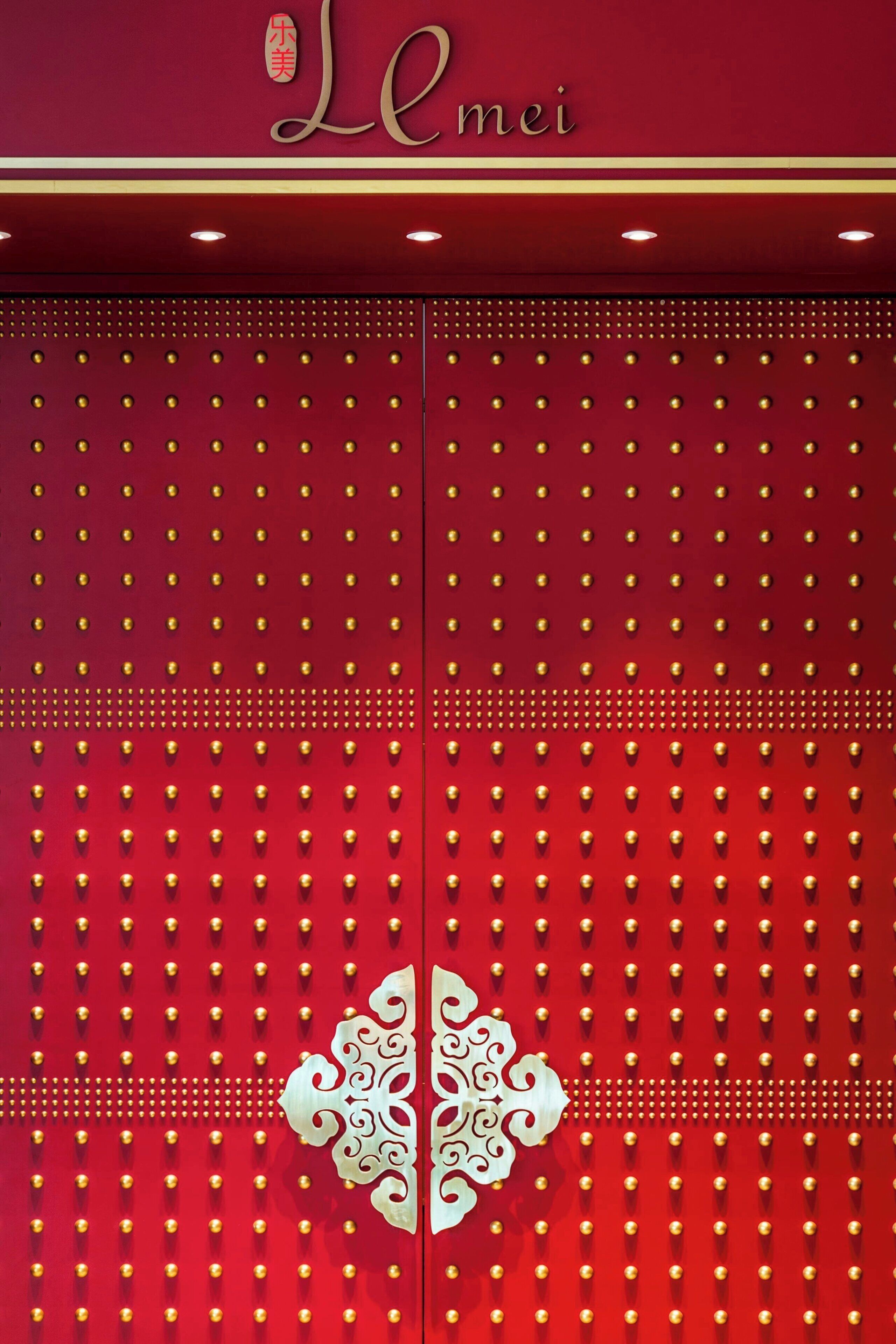 A red door with a decorative white emblem and the name "Lemei" above it.