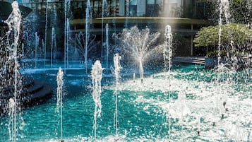 A fountain with multiple water jets in a pool, surrounded by a building with large windows.