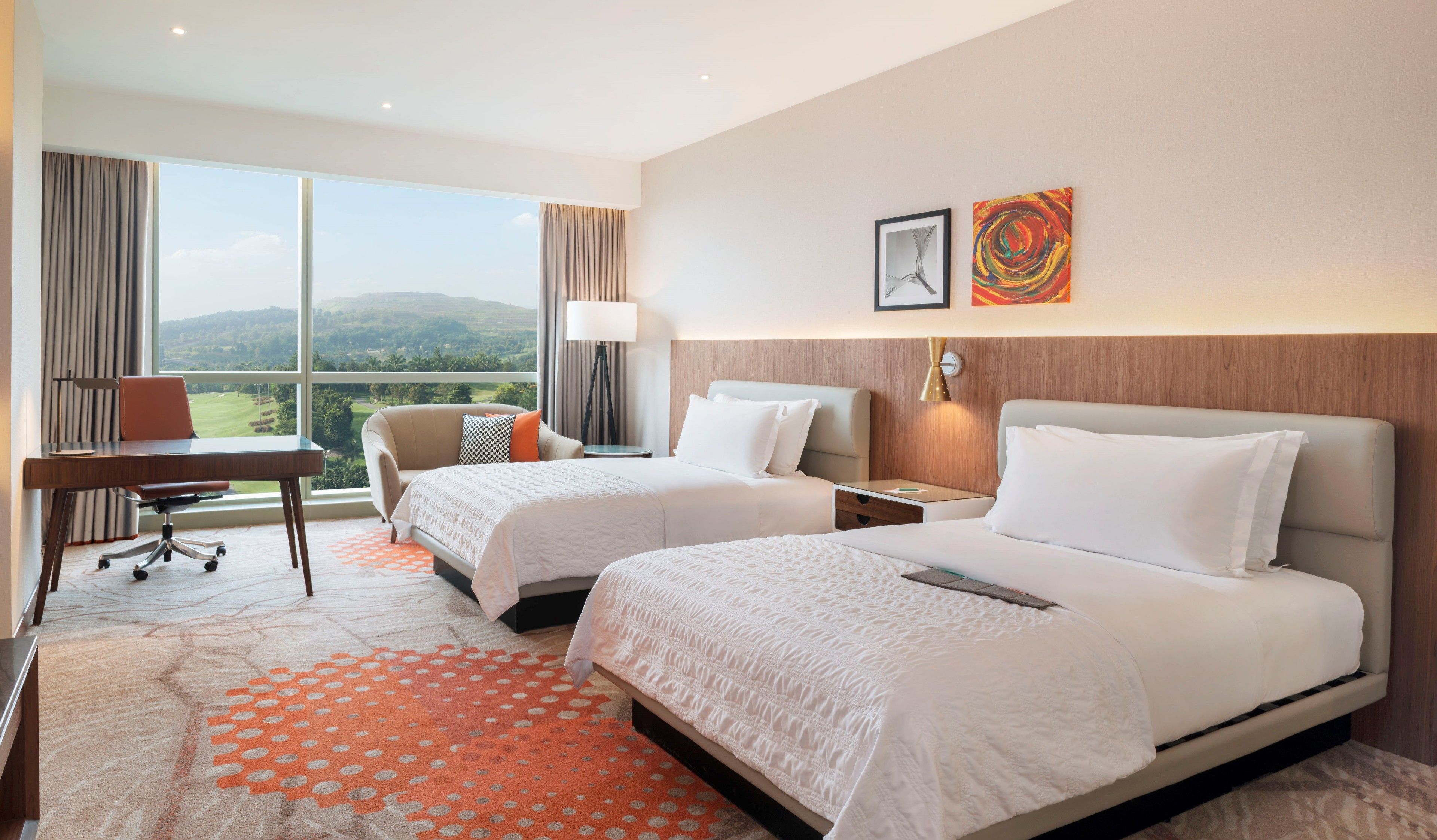 A hotel room with two beds, a desk, a chair, and a view of the outdoors.