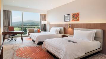 A hotel room with two beds, a desk, a chair, and a view of the outdoors.