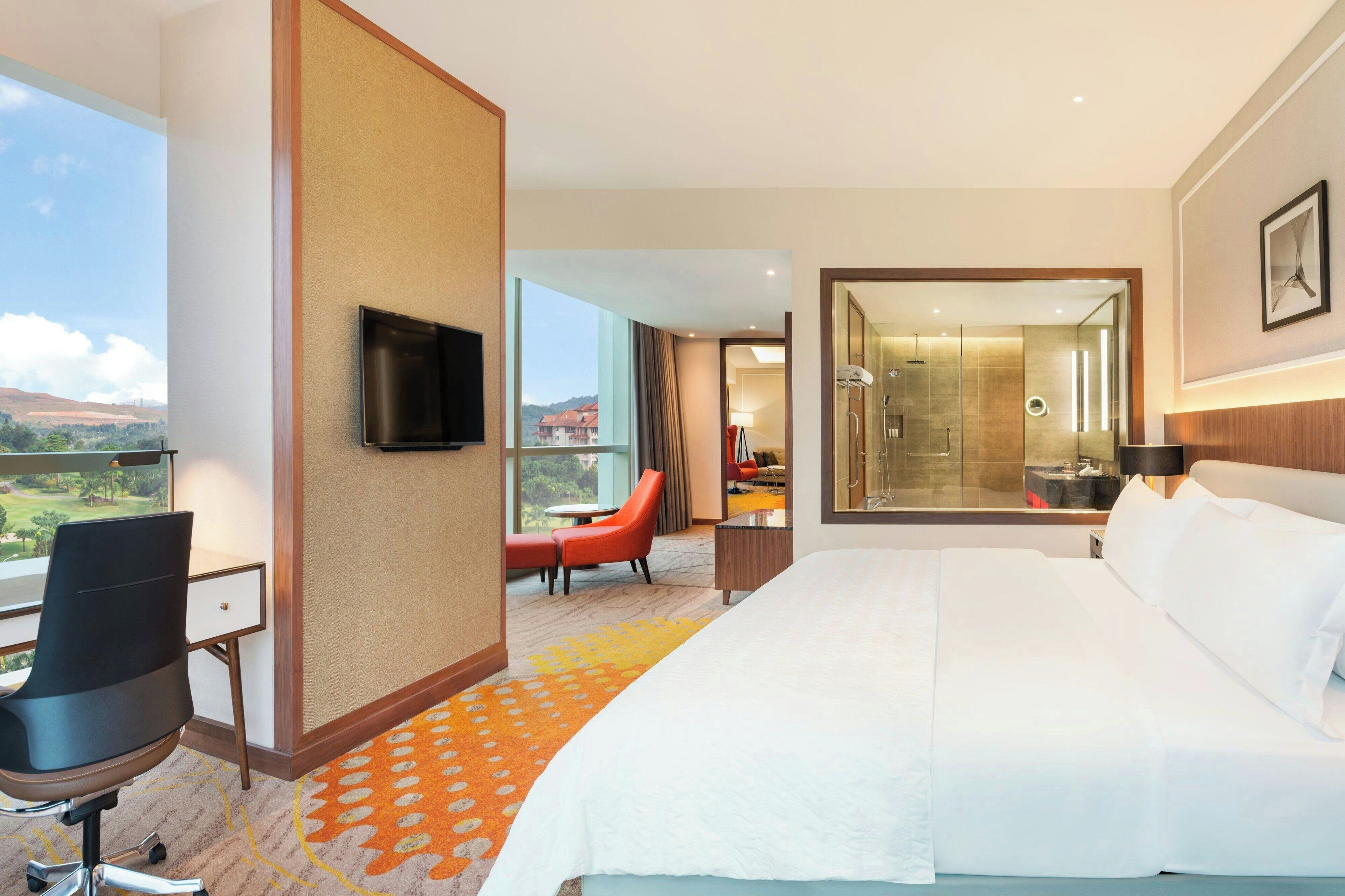 A hotel room with a large bed, a desk with a chair, a TV, and a view of the outdoors.