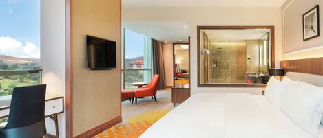 A hotel room with a large bed, a desk with a chair, a TV, and a view of the outdoors.