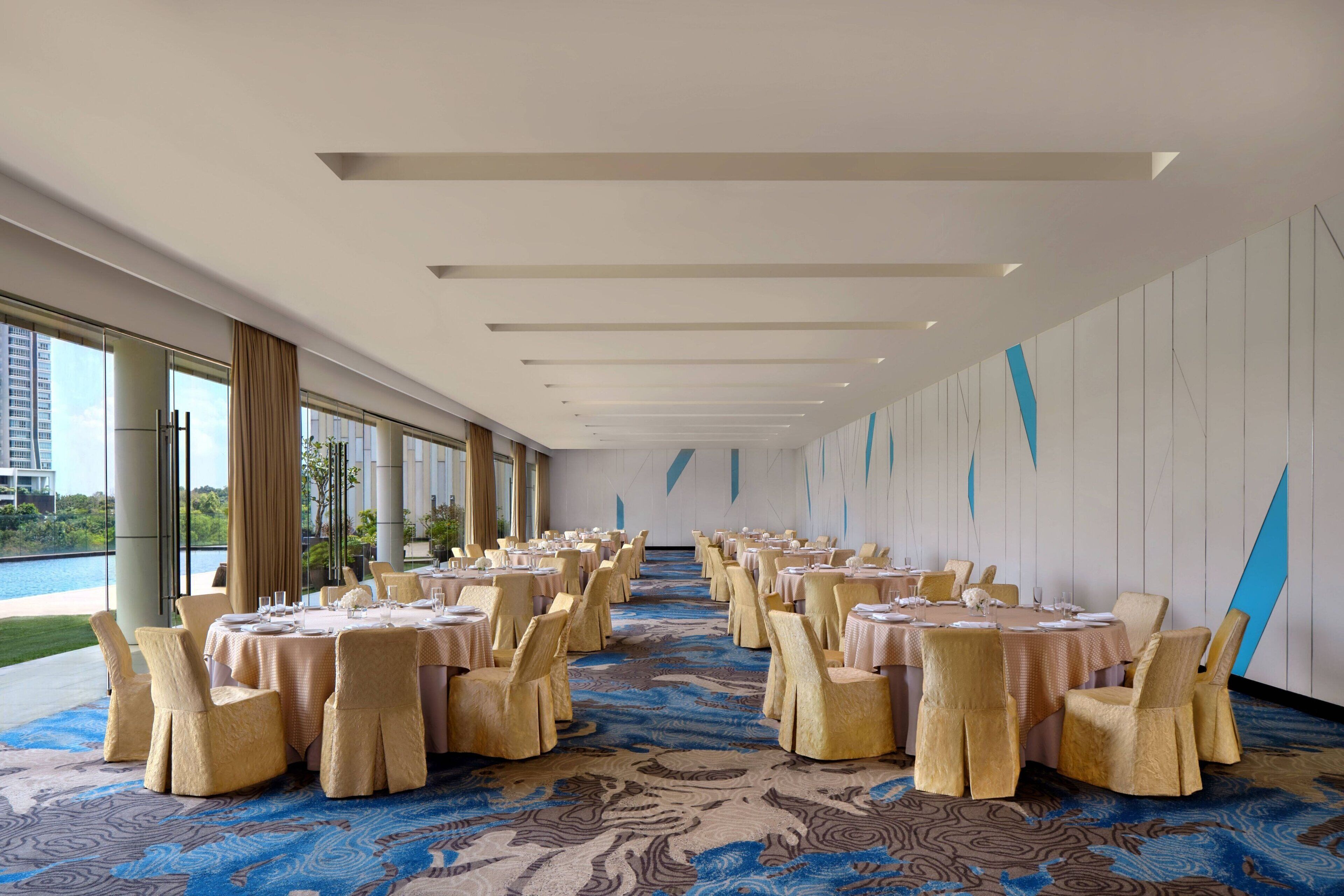 Une salle de banquet avec des tables rondes et des chaises, de grandes fenêtres et un tapis à motifs.