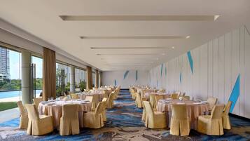Une salle de banquet avec des tables rondes et des chaises, de grandes fenêtres et un tapis à motifs.