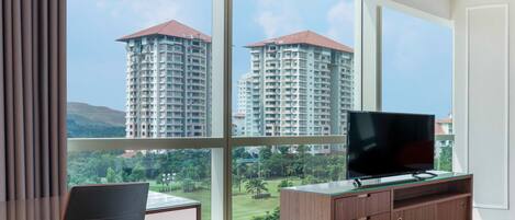 A hotel room with a large window, a desk, a chair, a TV on a wooden cabinet, and a bed.
