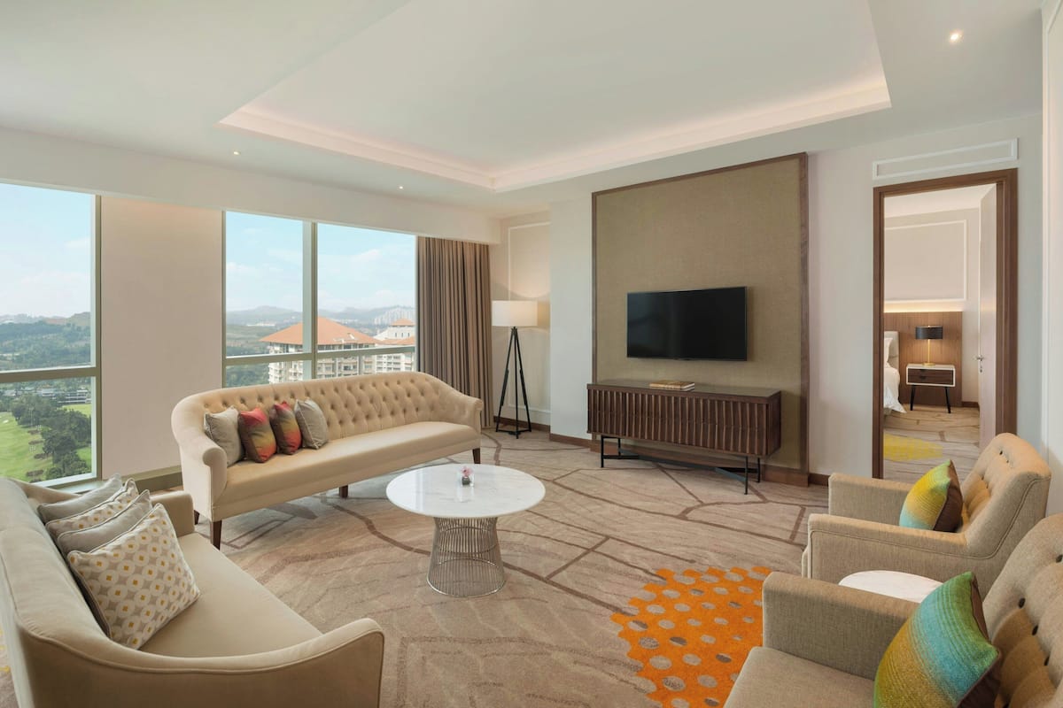 A modern hotel room with a large sofa, a television, and a view of the city.