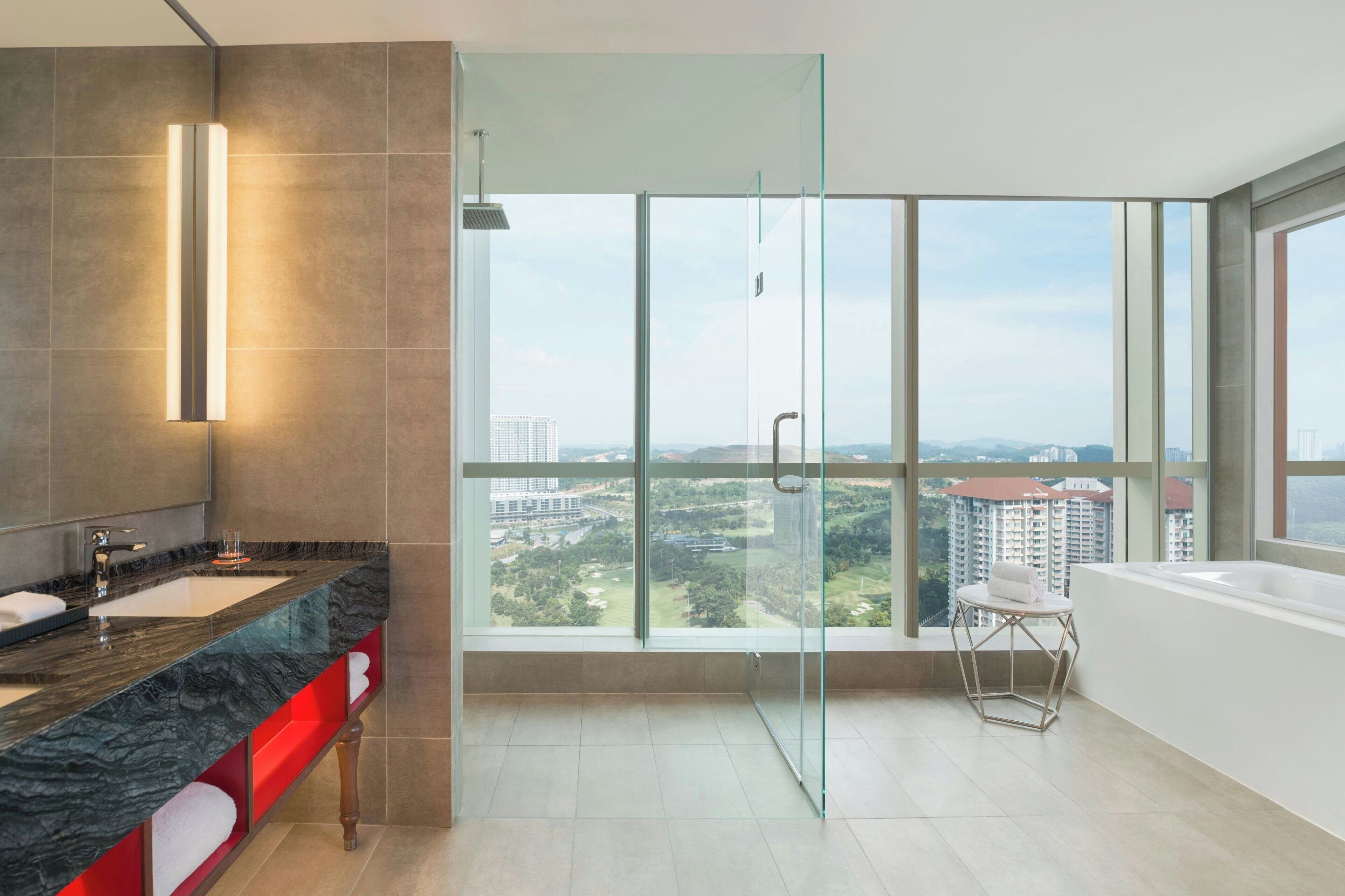 A modern bathroom with a glass shower enclosure, a large window offering a city view, and a separate bathtub area.