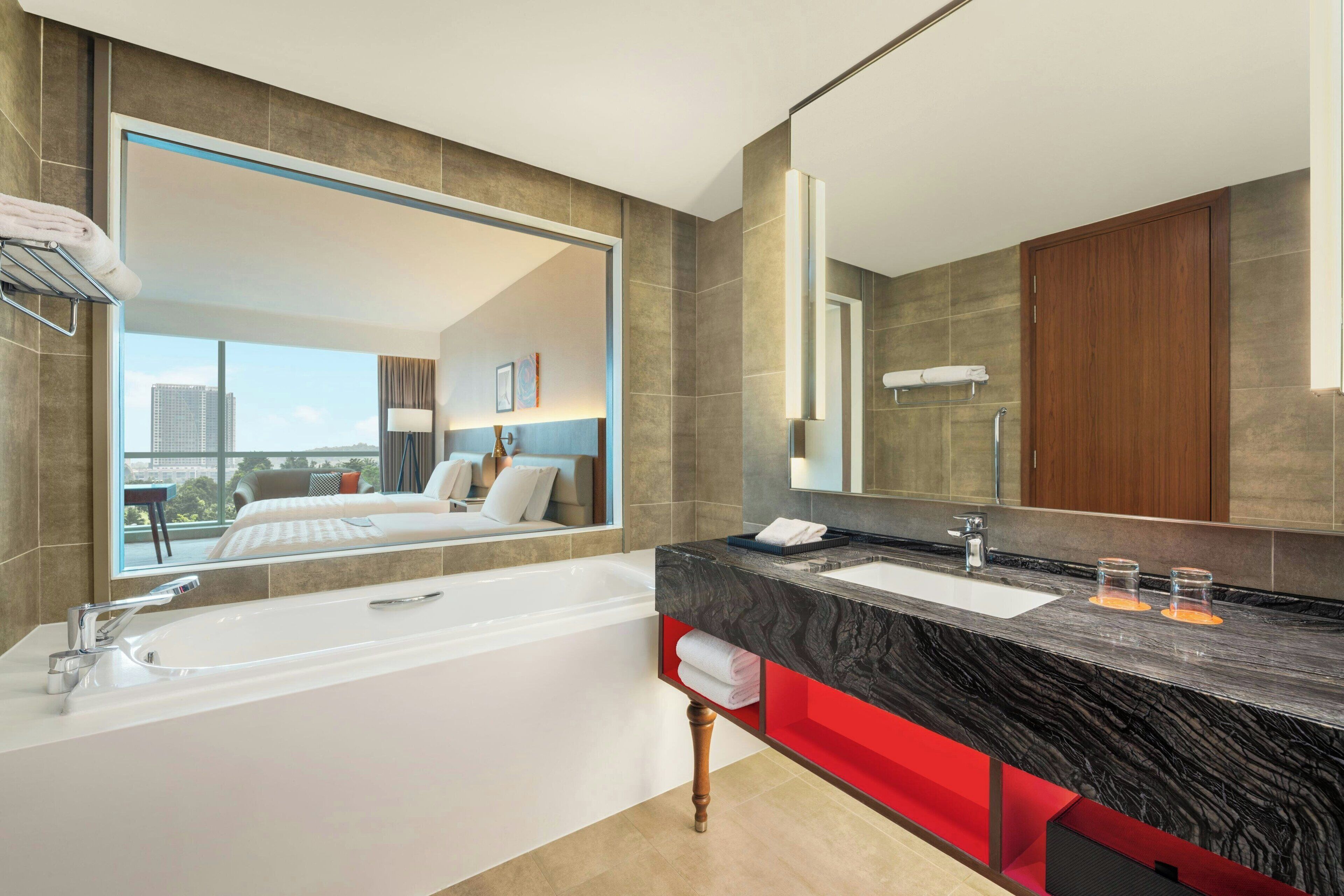 Une salle de bain moderne avec un grand miroir, une baignoire, un lavabo et un mur d’accent rouge.