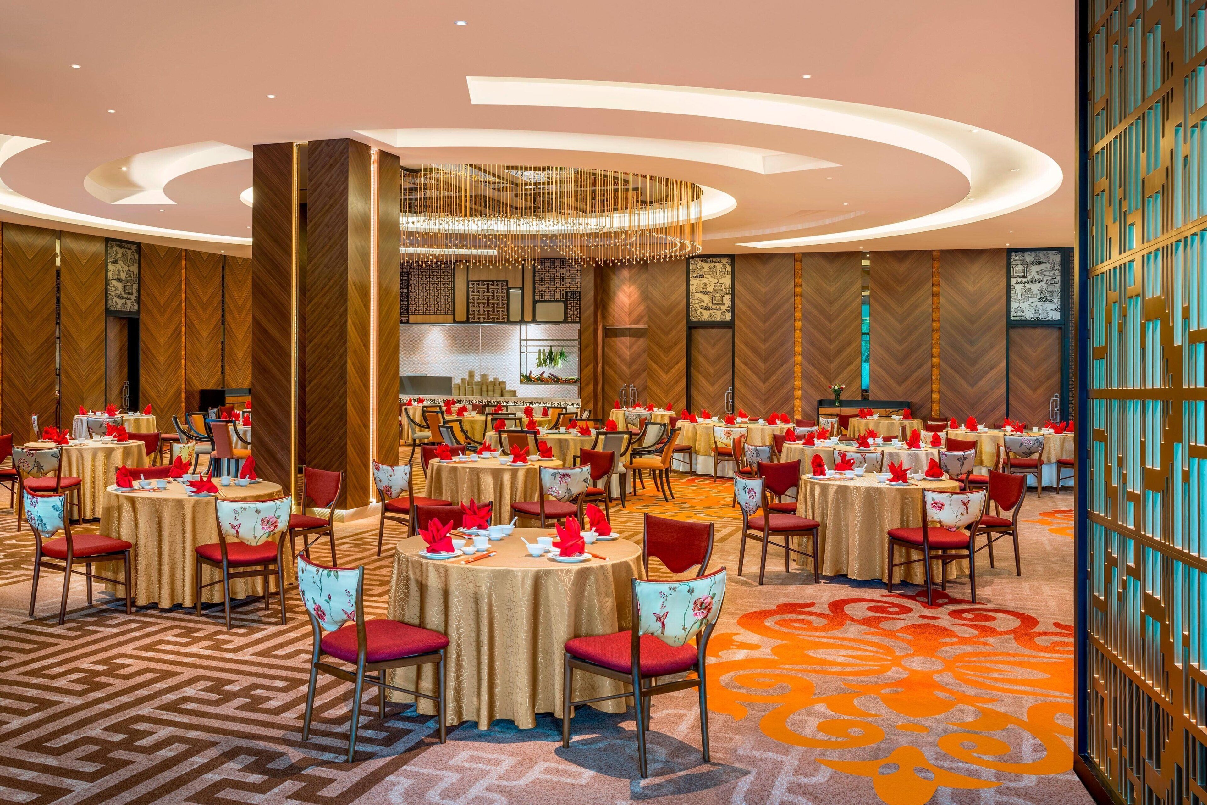 A large banquet hall with round tables, red chairs, and a patterned carpet.