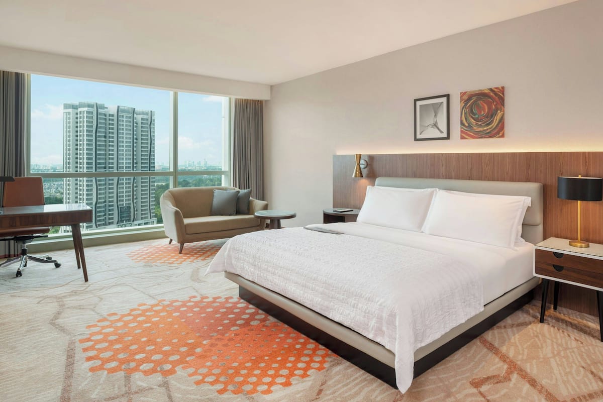 A hotel room with a large bed, a desk, a chair, and a view of high-rise buildings.