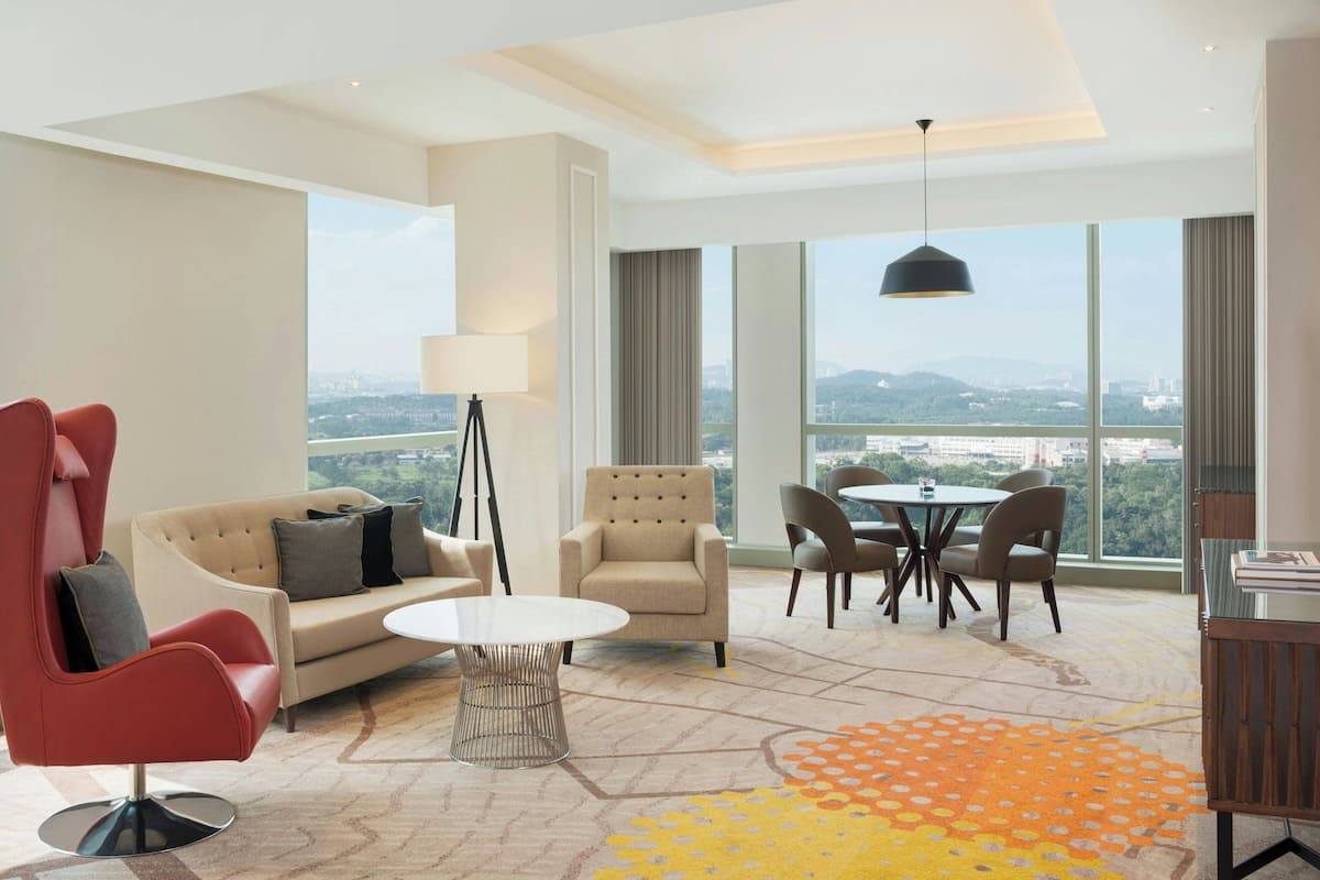 A modern hotel room with a sofa, armchair, dining table, and chairs.