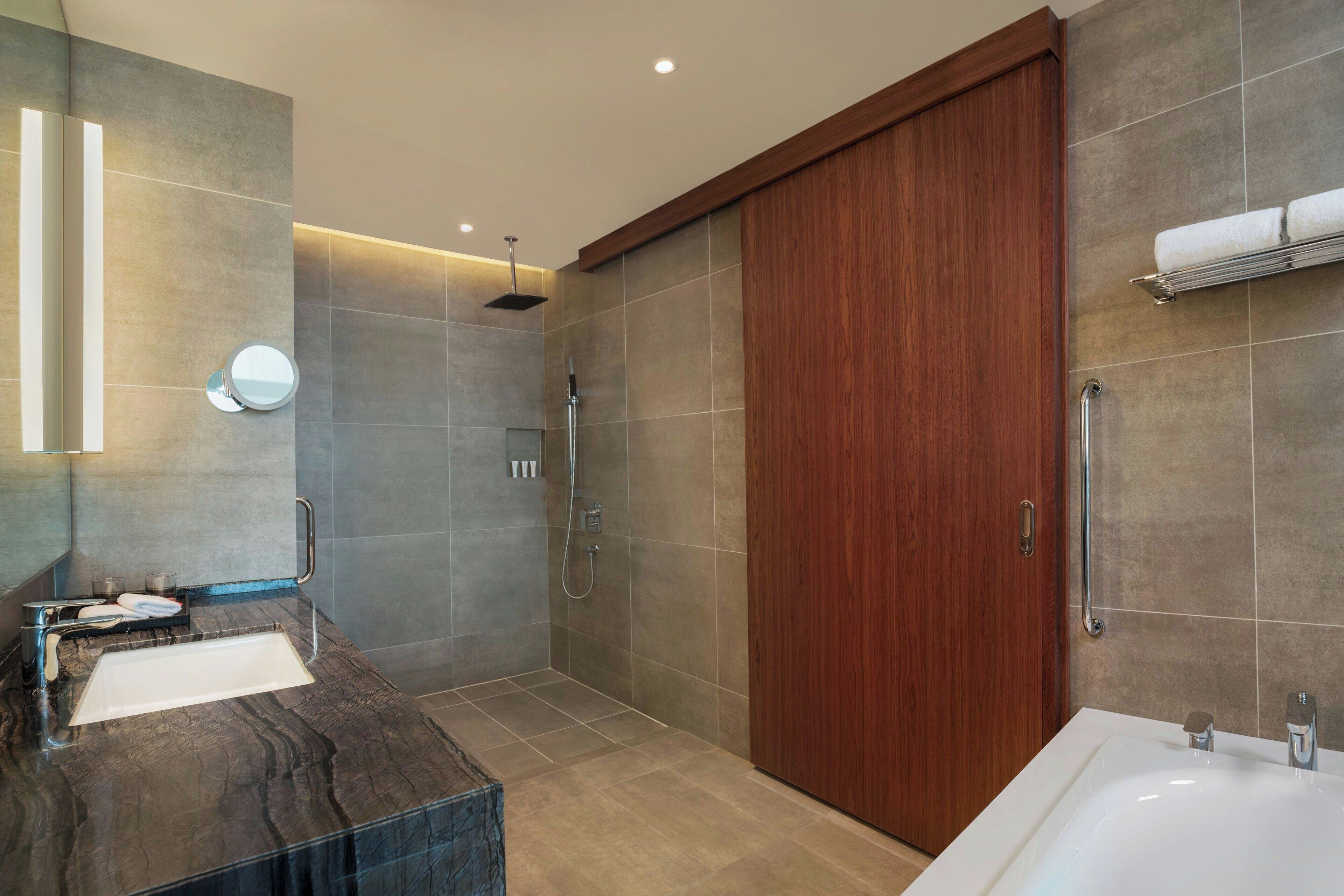 A modern bathroom with a large mirror, a sink, a shower, and a wooden door.